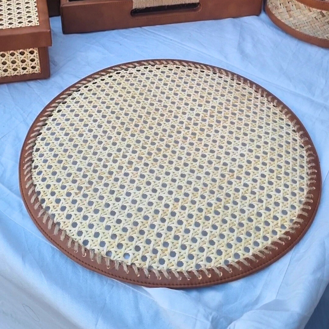 A round rattan table mat made of natural rattan cane with a brown vegan leather border, displayed on a blue background.