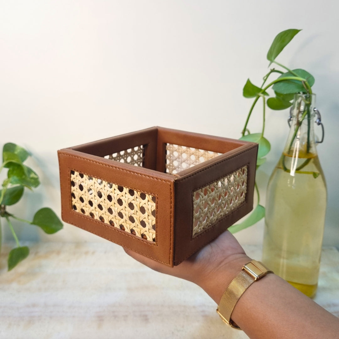 A mini square basket with a combination of brown color made from cane and vegan leather, held in a person's hand.