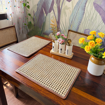 Rectangular rattan table mats placed on a wooden dining table with floral wallpaper in the background. The mats are beige with a woven pattern and have a rectangular shape.
